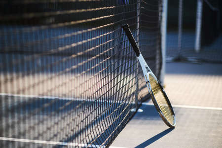 Tennis racquet is standing near tennis net outside at bright sunny day.の写真素材