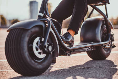 Man in black suit and shoes is sitting on electro bike while posing for photographer.の写真素材