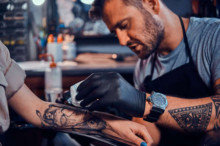 Dilligent focused tattoo artist is creating new tattoo on young womans hand at tatoo studio.の写真素材