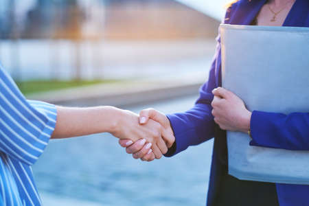 Two busy businesswomen have unformal meeting outside, they are greeting one each other with handshake.の写真素材