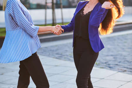 Two busy businesswomen have unformal meeting outside, they are greeting one each other with handshake.の写真素材