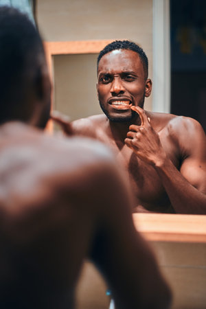Handsome african man is checking his teeth in the bathroom while see himself in the mirror.の写真素材