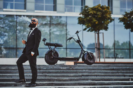 Pensive elegant businessman in sunglasses is smoking vaporiser making nice cloud.の写真素材