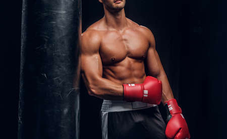 Attractive sporty man is posing with punching bag in dark photo studio.の写真素材