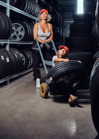 Strong female worker and her little helper have fun while looking for right tyres at warehouse.の写真素材