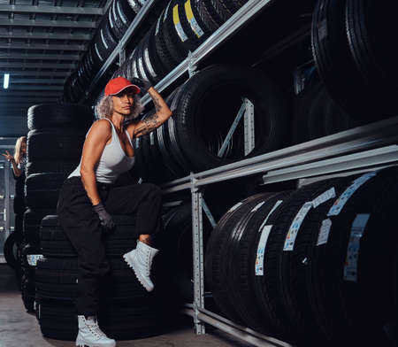 Sexy woman in red cap is chilling at tyre storage while posing for photographer.の写真素材