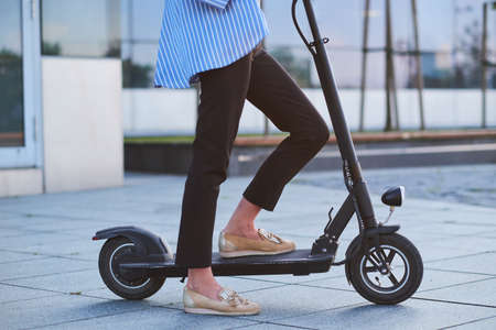 Young woman in stripped blaser is riding her new electrical scooter on the street.の写真素材