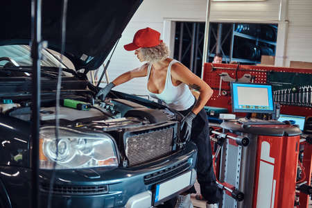 Manly strong woman is fixing cars engine with computer help at auto service.の写真素材