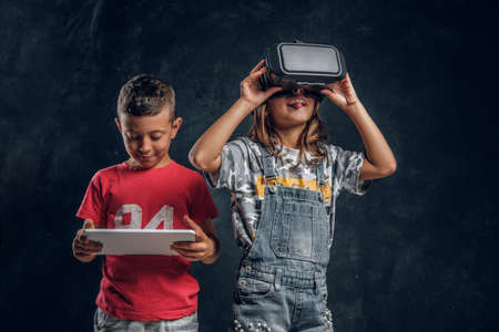 Happy smiling boy is holding tablet while funny girl is wearing vr goggles.の写真素材
