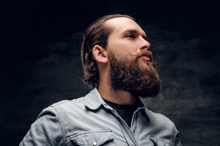 Groomed bearded man in light shirt is posing at dark photo studio.