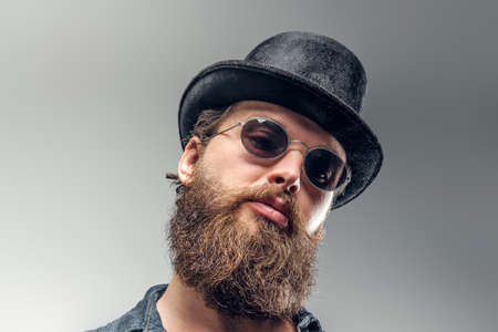 Serious bearded man in hat and sunglasses is posing at photo studio.の写真素材