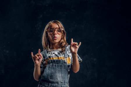Cute girl in big glasses is posing for photographer at dark photo studio.