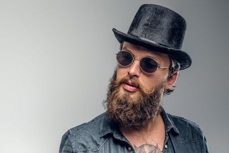 Serious bearded man in hat and sunglasses is posing at photo studio.