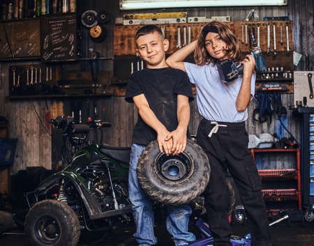 Pretty little kids are holding weel and screwdriver while posing for photographer at auto service.