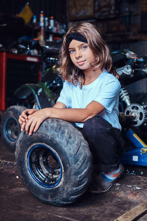 Nice small girl is posing for photographer with big wheel from car at auto service.の写真素材