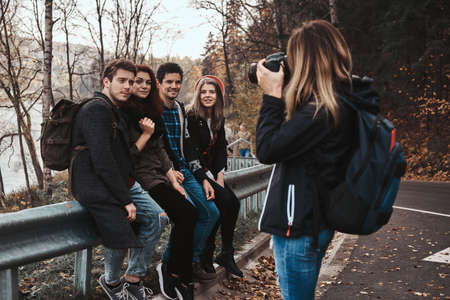 Young woman is taking a photo of her friends on digital camera at autumn forest.の写真素材