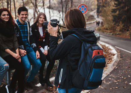 Young woman is taking a photo of her friends on digital camera at autumn forest.の写真素材