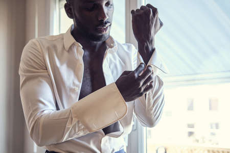 Focused young businessman is dressing up his vintage cufflinks while standing near window.の写真素材