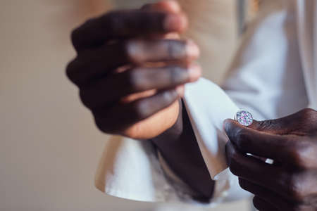 Closeup photo shoot of african american man in white shirt with diamond cufflink in hand.の写真素材