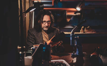 Pensive shoe master in glasses is working on his new shoes collection at his workshop.の写真素材