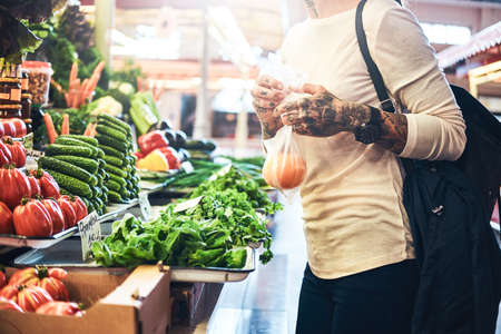 Tattooed woman is buying fresh seasonal vegetables at her local farmers marketplace.の写真素材