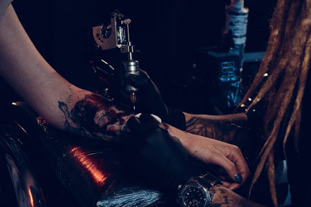 Dark toned photo of process of tattooing by experienced master.