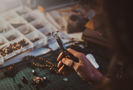 Creative woman is holding pliers and crystal clear quartz in it.