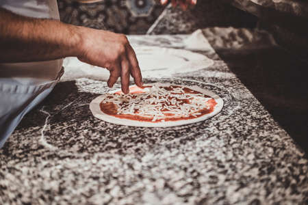 Experienced chef is adding cheese for his freshly made italian pizza.の写真素材