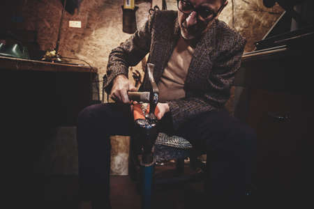 Focused mature cobbler is fixing sole for boots using hammer.の写真素材