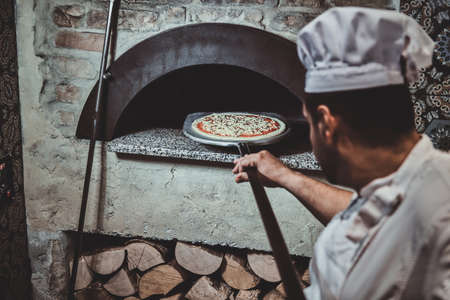 Experienced chef is putting his pizza to the oven using special giant spatula.の写真素材
