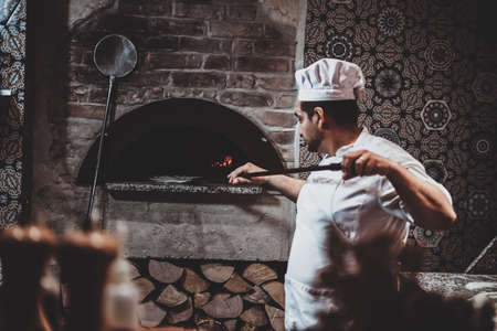 Experienced chef is putting his pizza to the oven using special giant spatula.の写真素材