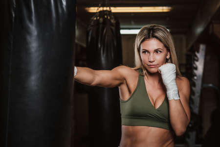 Muscular pretty woman is doing her kickboxing exercises with punching bag.
