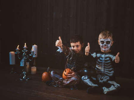Good little friends in Halloween costumes are sitting on the floor with pumpkins and candles.の写真素材