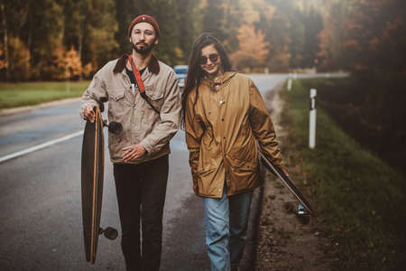 Attractive romantic couple is walking on the road surrounded with autumn trees while holding their...