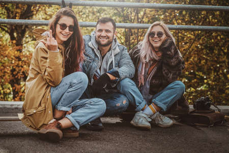 Pretty cheerful girl is showing middle finger while sitting in autumn park with her friends.の写真素材