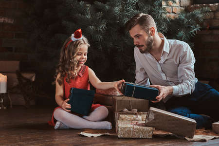 Happy wondered father is receiving gift from his little daughter while sitting under christmas tree.の写真素材