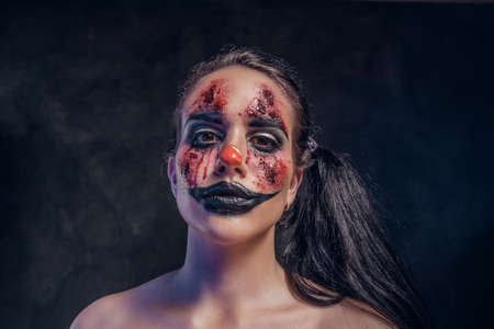 In smoky dark photo studio woman in a role of evil clown is posing for photographer.の写真素材