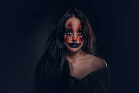 Portrait of young woman in a role of evil scary clown at dark photo studio.の写真素材