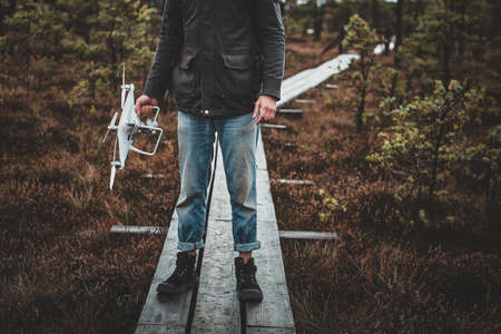 Young hipster in blue denim jeans is standing on wooden path with drone in hand.の写真素材