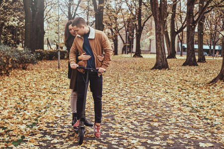 Attractive couple has a nice romantic walk at autumn park with scooter.の写真素材