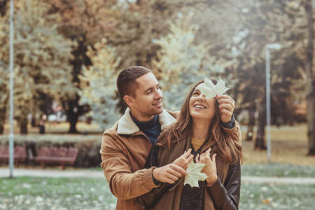 Happy smiling romantic people have fun with maple leaf at autumn park.の写真素材