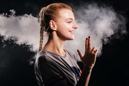 Happy smiling girl is showing gun with fingers at dark photo studio, surrounded with smoke.の写真素材