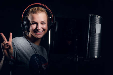 Happy smiling rockstar in headphones is recording her song at audio studio.