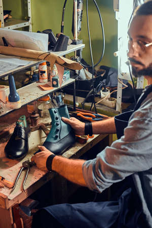 Experienced shoemaker is creating retro leather shoes at his comfortable workshop.
