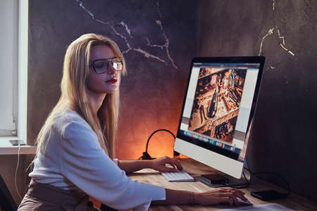 Attractive blond girl is studying at her modern room using computer.の写真素材