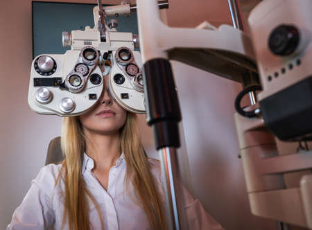 Optometry concept - pretty young woman having her eyes examined by eye doctor.