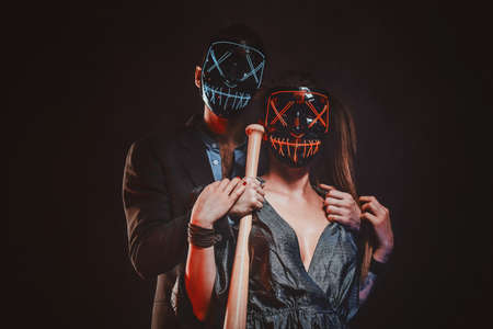 Elegant man with baseball bat in hand is hugging his sexy woman, both of them are wearing masks.の写真素材