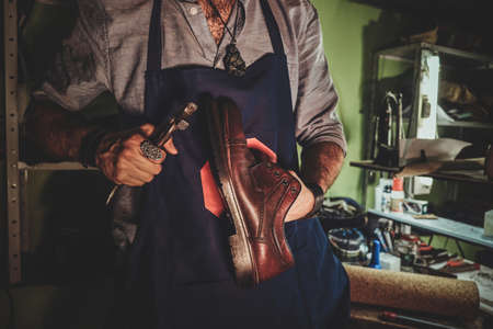 Diligent cobbler is working on shoe sole using special tool at his dark workplace.の写真素材