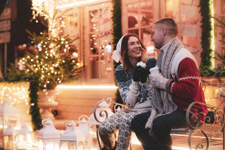 charming couple  are enjoying hot drinks while sitting on the bench.の写真素材