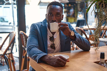 Afro american businessman is enjoying his tasty coffee while sitting at cafe.の写真素材